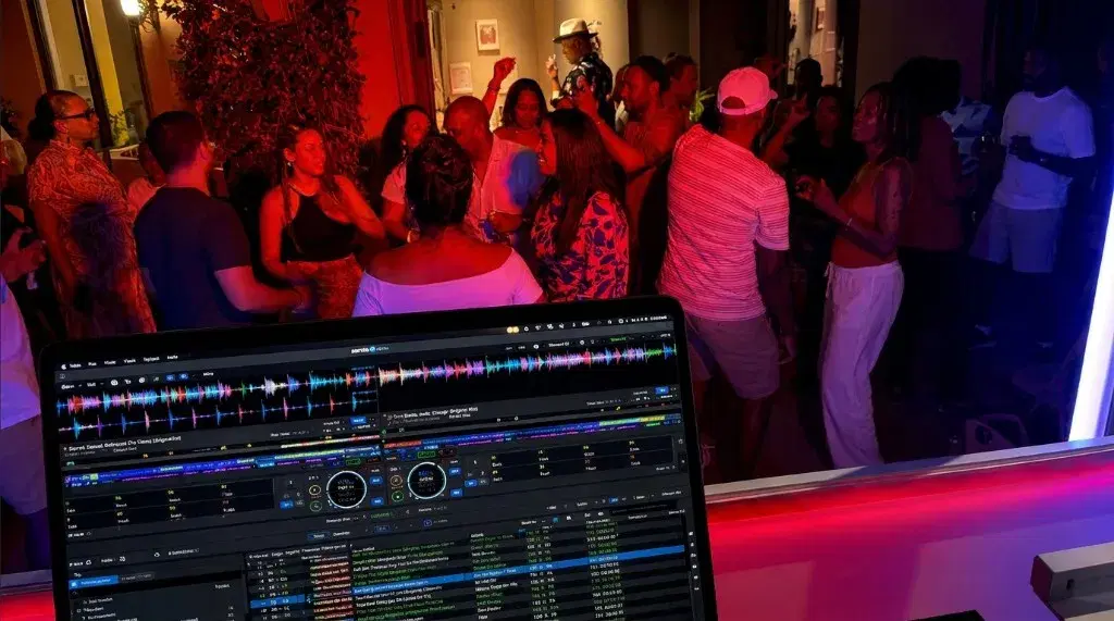 Guests dancing next to the DJ booth under red lighting, with the laptop in front